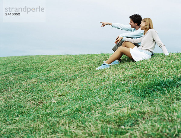 Paar sitzt auf Gras und schaut in die Ferne.