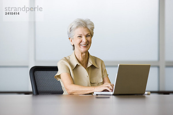 Seniorin am Schreibtisch sitzend  mit Laptop  lachend