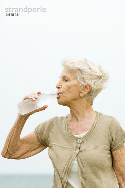 Seniorenfrau trinkt Flasche kaltes Wasser