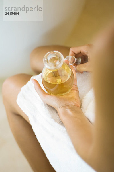 Frau in Handtuch gewickelt  mit einem Glas Massageöl  beschnitten