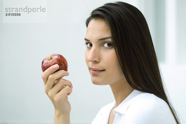 Frau hält Apfel  schaut seitwärts in die Kamera