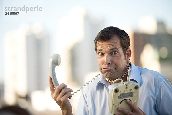 Mann mit Festnetztelefon  Kabel um den Hals gewickelt  Blick auf die Kamera