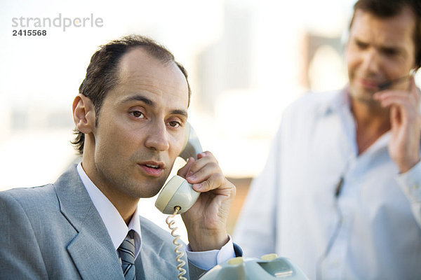 Geschäftsmann über Festnetztelefon  Mann im Hintergrund über Headset
