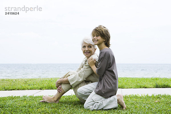 Großmutter und Enkel sitzen zusammen im Freien  lächelnd  Meer im Hintergrund