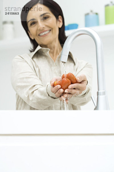 Frau spült Roma-Tomaten unter Wasserhahn  lächelt in die Kamera