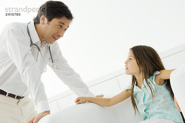 Der Arzt beugt sich vor  redet mit dem kleinen Mädchen.