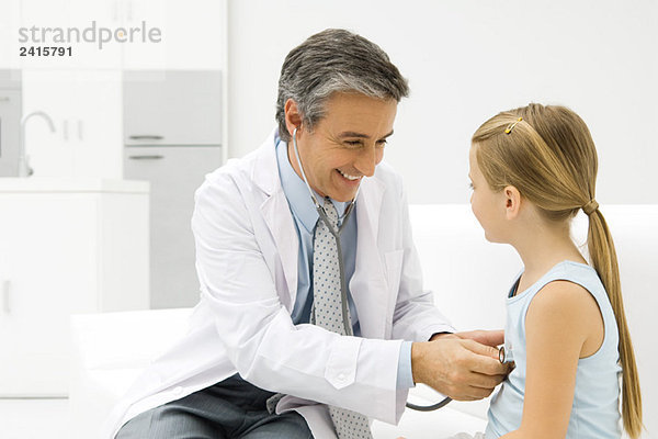 Arzt hört auf das Herz des kleinen Mädchens mit Stethoskop  lächelnd