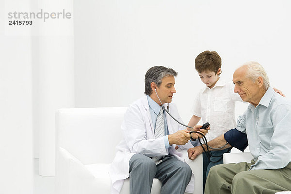 Arzt  der den Blutdruck eines älteren Mannes misst  Junge  der zuschaut.