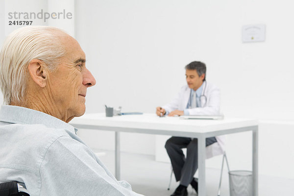 Arzt am Schreibtisch  Schwerpunkt Senior Patient im Vordergrund
