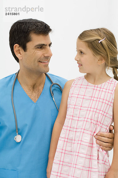 Arzt mit Arm um die Taille des kleinen Mädchens  beide lächeln einander an.