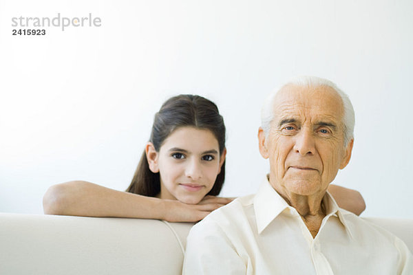 Älterer Mann lächelt in die Kamera  die Enkelin schaut ihm über die Schulter.