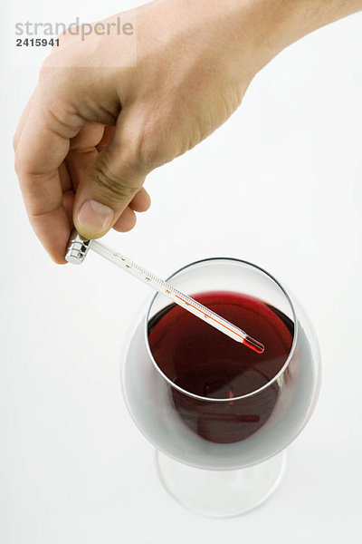Person hält Thermometer über Glas Rotwein  abgeschnittene Handansicht