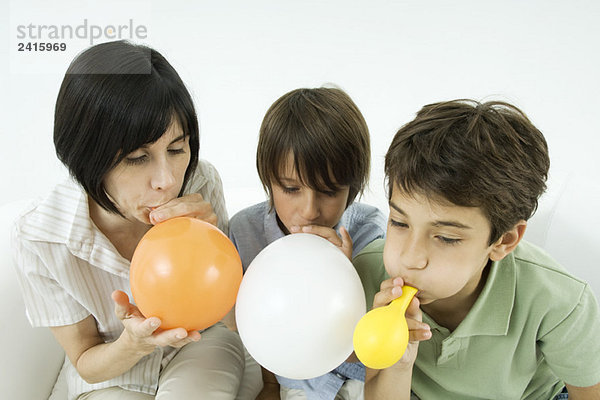 Mutter und zwei Söhne beim Aufblasen von Luftballons