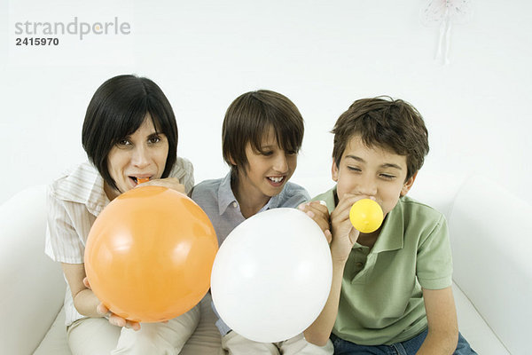 Mutter und zwei Söhne  die Luftballons aufblasen  lächelnd  Frau mit Blick auf die Kamera