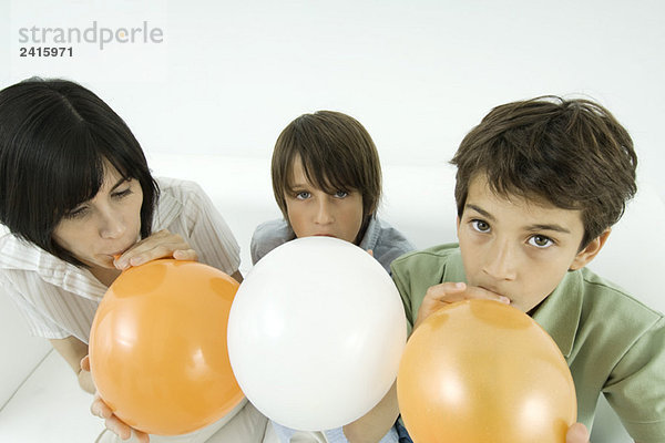 Mutter und zwei Söhne beim Aufblasen von Luftballons  Jungen beim Blick in die Kamera