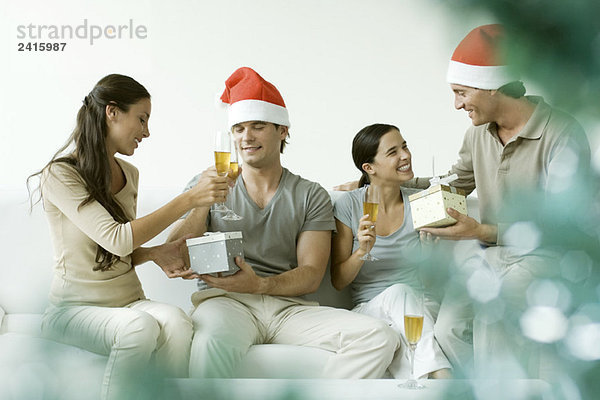 Zwei Paare tauschen Weihnachtsgeschenke aus  trinken Champagner  Männer mit Weihnachtsmützen