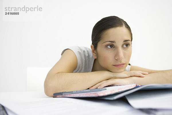 Junge Frau sitzend mit Notizbuch  Kopf auf den Armen liegend  wegschauend