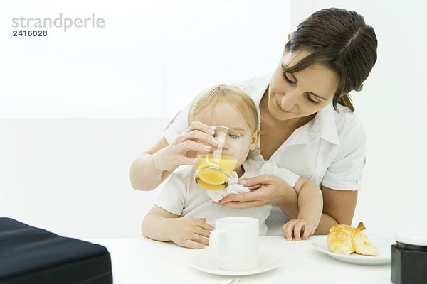 Frau hilft Baby trinken aus Glas Saft