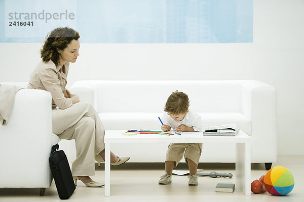 Junge berufstätige Frau mit Aktentasche im Wartezimmer sitzend  während Sohn Farben
