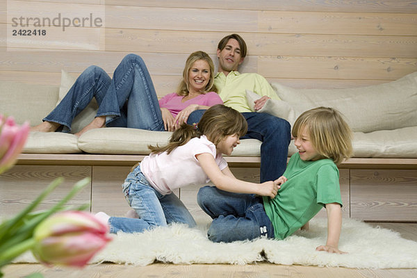 Junge (8-9) und Mädchen (6-7) kämpfen auf Teppich  Eltern im Hintergrund  Porträt
