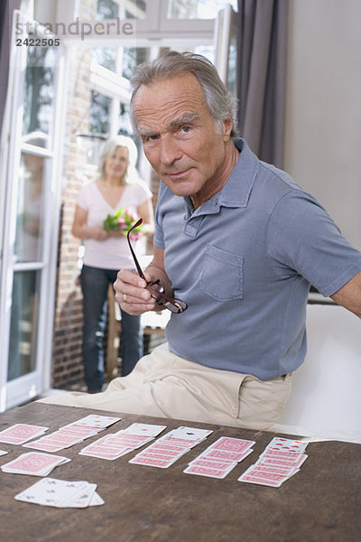 Senior Mann spielt Solitär  Senior Frau steht in der Tür  Porträt