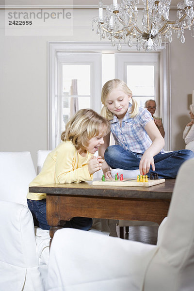 Junge (8-9) und Mädchen (8-9) beim gemeinsamen Spielen  Großeltern im Hintergrund