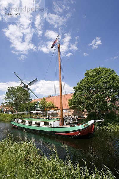 Segelboot in Kanal mit industriellen Windmühle im Hintergrund  Ostgrossefehn  Niedersachsen  Deutschland