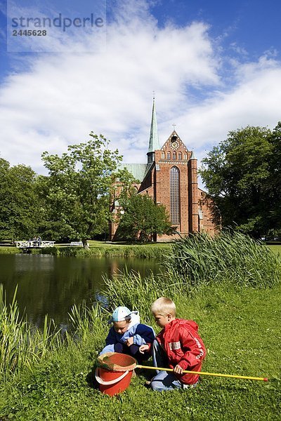 Zwei Kinder spielen an Teich Seite mit Kirche im Hintergrund  Bad Doberan  Mecklenburg-Vorpommern Deutschland