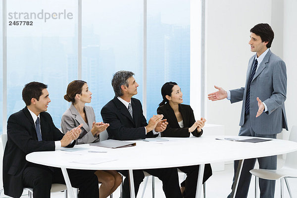 Geschäftsleute applaudieren der Präsentation des Mitarbeiters  sitzen um den Tisch herum
