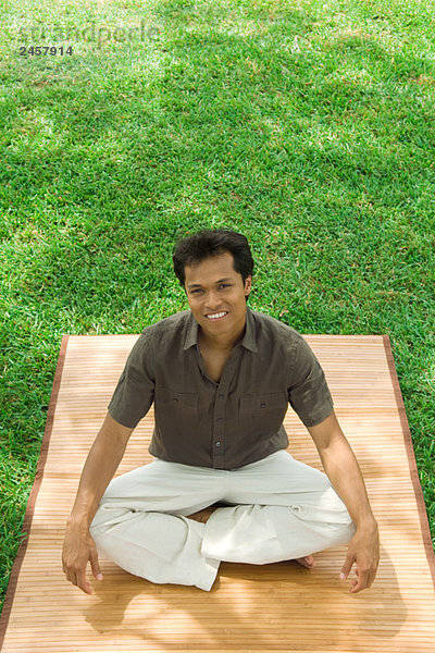 Mann im Schneidersitz im Freien  lächelnd vor der Kamera  hoher Blickwinkel