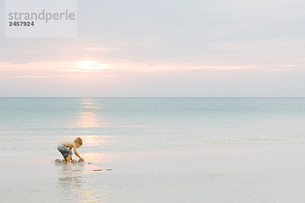 Kleiner Junge spielt am Strand bei Sonnenuntergang  Seitenansicht  volle Länge