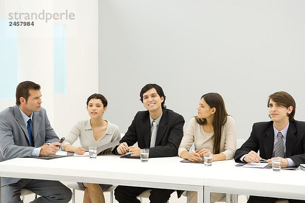 Gruppe von Geschäftspartnern sitzt am Konferenztisch  schaut weg  lächelt