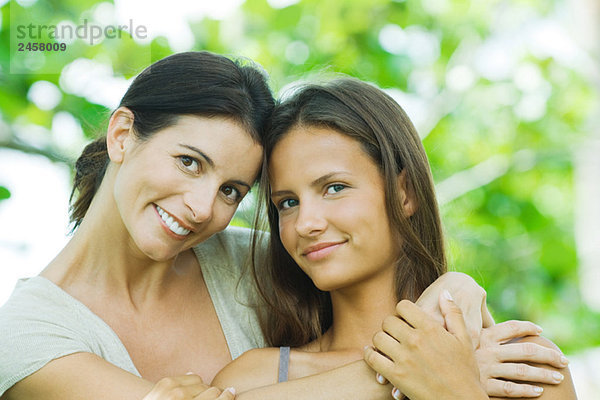 Mutter umarmt Teenagertochter  beide lächelnd vor der Kamera  Porträt