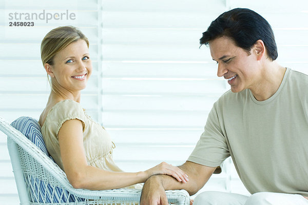 Paar auf der Veranda sitzend  Frau berührt den Arm des Mannes und lächelt in die Kamera  Mann schaut hinunter
