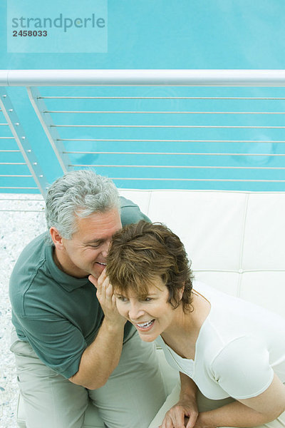 Paar auf dem Balkon sitzend  Mann flüstert ins Ohr der Frau  Blick in den hohen Winkel