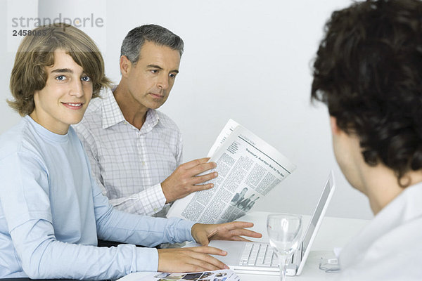 Teenager Junge am Tisch mit Vater  mit Laptop-Computer  Mann Zeitung lesen