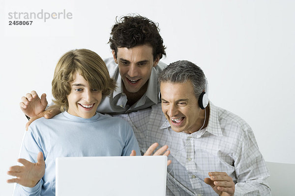 Vater und zwei Söhne schauen gemeinsam auf den Laptop  lächelnd  die Hände erhoben