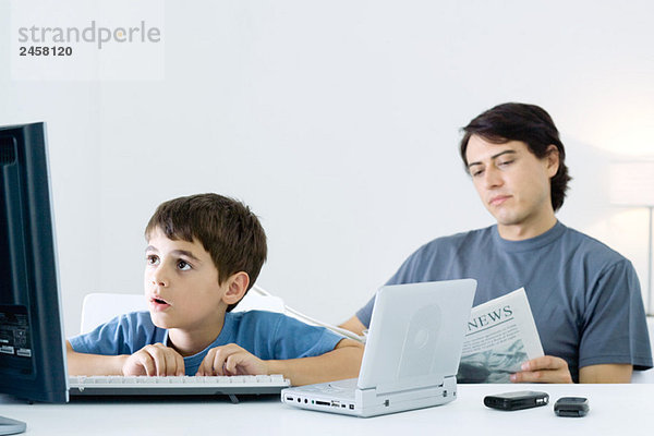 Kleiner Junge Computer und tragbarer DVD-Player  Vater liest Zeitung im Hintergrund