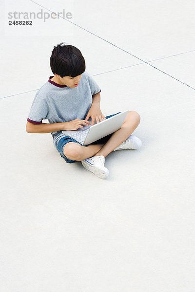 Junge sitzt im Schneidersitz auf dem Boden  mit Laptop