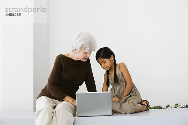 Seniorin und Enkelin benutzen zusammen einen Laptop und schauen nach unten.