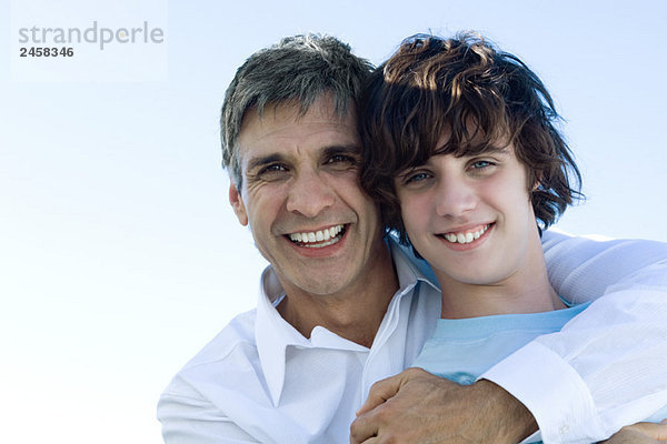 Vater umarmt seinen Sohn von hinten  lächelt in die Kamera  Porträt