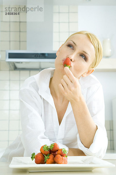 Frau hält Erdbeere an die Lippen  schaut nach oben  Stapel Erdbeeren auf einem Teller  Mund