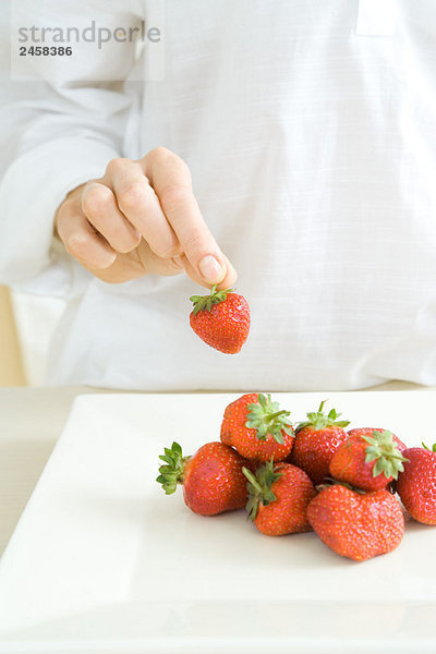 Hand  die eine Erdbeere von einem Stapel auf der Theke aufhebt.