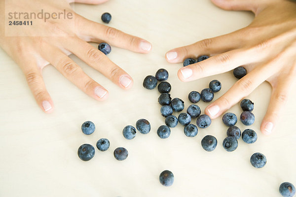 Paar Hände mit weit ausgebreiteten Fingern über verstreuten blauen Beeren