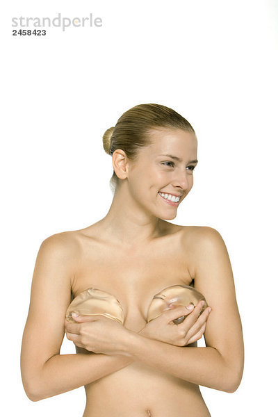 Nackte Frau  die Brustimplantate über der Brust hält  lächelnd