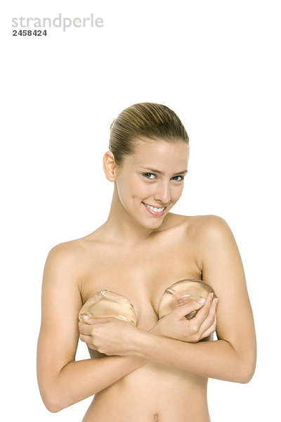Nackte Frau mit Brustimplantaten über der Brust  lächelnd in der Kamera