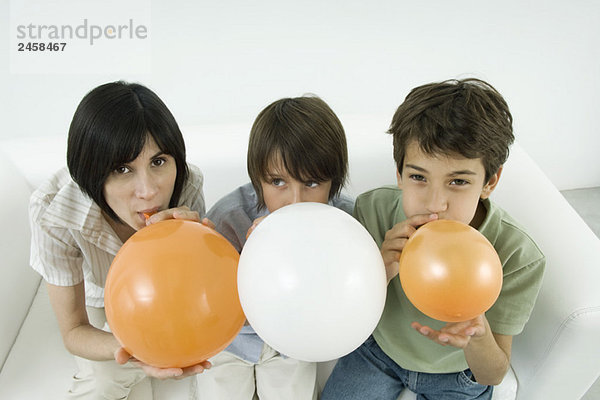 Mutter und zwei Söhne  die Luftballons aufblasen  Frau und ein Sohn schauen in die Kamera.