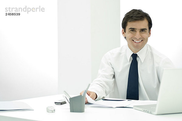 Männlicher Profi am Schreibtisch sitzend  lächelnd vor der Kamera