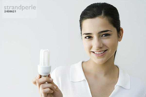 Junge Frau mit Energiesparlampe  lächelnd vor der Kamera