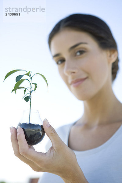 Frau hält Topfpflanzen  lächelt in die Kamera  fokussiert auf den Vordergrund